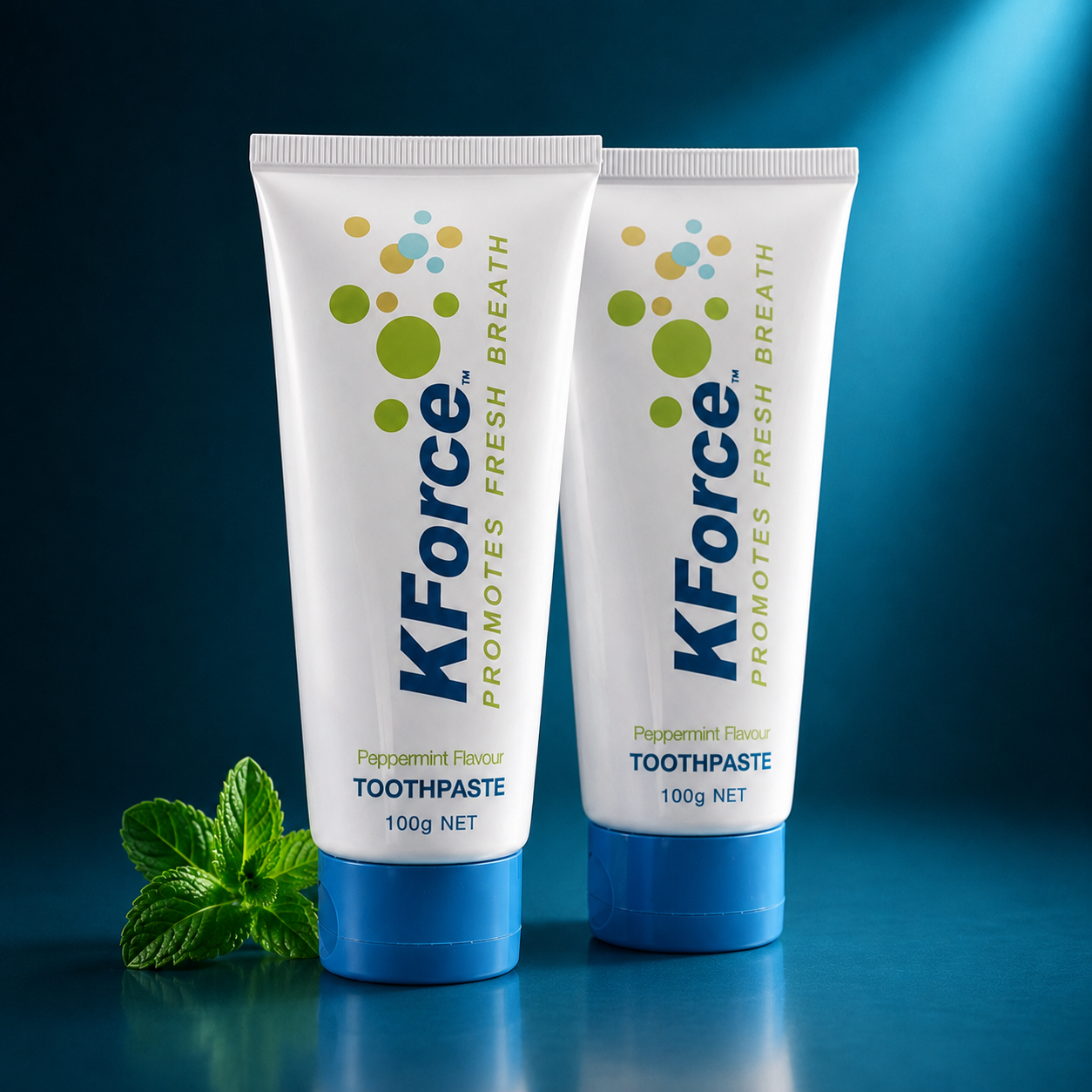 Two tubes of KForce toothpaste standing upright on a dark blue surface against a blue gradient background, with a small mint leaf placed at the base of the left tube.